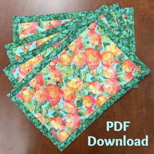 May include: A stack of floral placemats with a watercolour design. The placemats feature a pattern of orange and yellow roses on a turquoise background, framed by a green leaf border. The text "PDF Download" is visible.