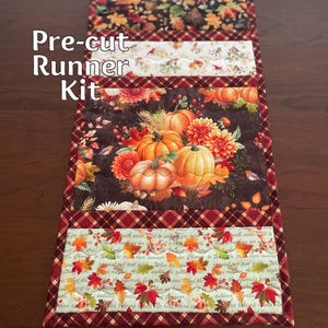 May include: A pre-cut runner kit featuring a fall theme. The design includes pumpkins, flowers, and autumn leaves in shades of orange, brown, and red. The text "Pre-cut Runner Kit" is visible on the top left.
