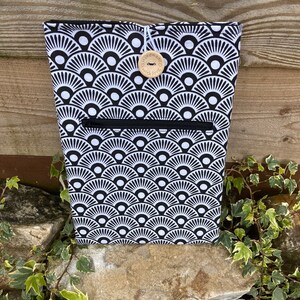 Op de afbeelding: Zwarte en witte geometrische geprinte ritszak met een houten knoop waarop "Handmade with love" staat.