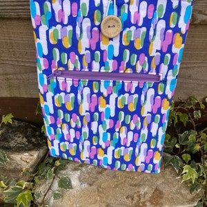 May include: A blue fabric pouch with a zipper closure and a wooden button that says "handmade with love". The pouch has a colorful abstract pattern with pink, yellow, green, and blue shapes.