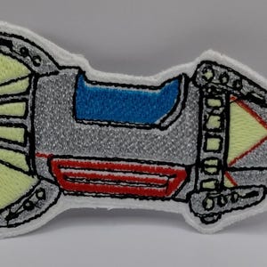 May include: Embroidered patch of a retro-style spaceship. The patch features a silver body with blue, red, and yellow accents. The spaceship has a white border and black outline.