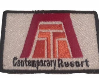 May include: Rectangular patch with a white background and a black border. The patch features a stylized logo in red and orange, with the words "Contemporary Resort" in black text below the logo.