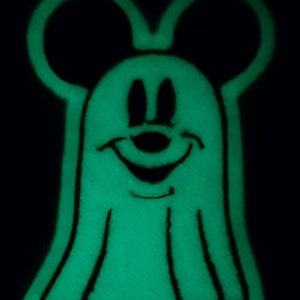 May include: A green glow-in-the-dark ghost with Mickey Mouse ears and a smiling face.