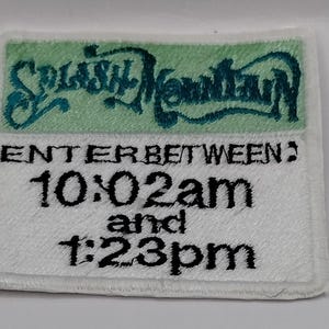May include: A rectangular embroidered patch with a white background. The top section features the text Splash Mountain in dark teal script on a light green field. Below, black text reads ENTER BETWEEN: 10:02am and 1:23pm in a bold font.