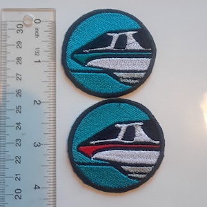May include: Two embroidered patches with a teal border and a black background. The patches feature a white and gray boat design with either a green or red accent. The patches are approximately 2 inches in diameter.