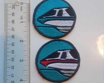 May include: Two embroidered patches with a teal border and a black background. The patches feature a white and gray boat design with either a green or red accent. The patches are approximately 2 inches in diameter.