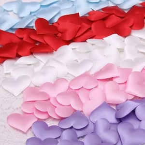 May include: A collection of heart-shaped fabric petals in various colors, including light blue, red, white, pink, and purple. The petals are arranged in rows, creating a gradient effect. Ideal for crafts, decorations, or special events.