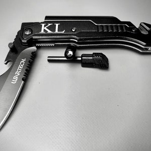 May include: A black multi-tool knife with a serrated blade, bottle opener, and a fire starter. The knife is open and the blade is visible. The knife is engraved with the initials "KL".