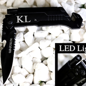 May include: Black multi-tool knife with a built-in LED light. The knife has a bottle opener, a serrated blade, and a safety belt cutter. The knife is engraved with the initials "KL".