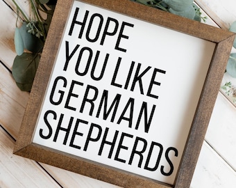 Może przedstawiać: Kwadratowy drewniany znak z ciemnobrązową ramą i białym panelem środkowym. Tekst HOPE YOU LIKE GERMAN SHEPHERDS jest wydrukowany pogrubionymi czarnymi wielkimi literami na białym tle. Znak jest ustawiony pod kątem na płaskiej powierzchni.