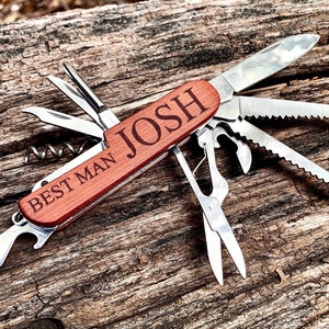May include: A multi-tool pocket knife with a wooden handle engraved with the text "Best Man Josh". The knife has a variety of tools, including a blade, a saw, a bottle opener, and a corkscrew.