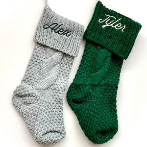 May include: Two knitted Christmas stockings with personalized names, one gray with "Alex" and one green with "Tyler", hanging on a white background.