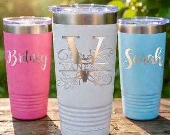 May include: Three personalized stainless steel tumblers in pink, white, and light blue. The pink tumbler has the name "Britney", the white tumbler has the name "Vanessa" with a decorative initial, and the blue tumbler has the name "Sarah".