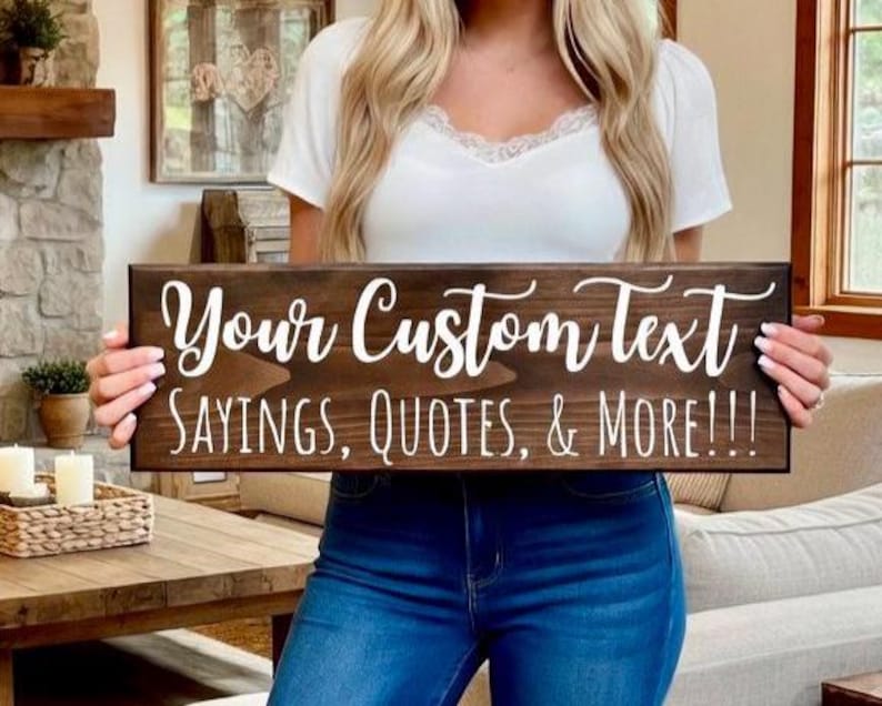 Peut inclure: Une enseigne en bois brun fonc&eacute; avec du texte blanc en cursive qui dit "Your Custom Text SAYINGS, QUOTES, & MORE!!!". L'enseigne rectangulaire est tenue par une personne portant un haut blanc et un jean bleu.