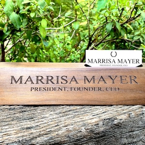 May include: A wooden desk nameplate with the name "Marrisa Mayer" engraved on it. The nameplate also includes the title "President, Founder, CEO".