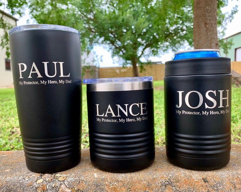 May include: Three black stainless steel tumblers with personalized names and the text "My Protector, My Hero, My Dad". The tumblers are on a stone surface.