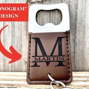 May include: A brown leather bottle opener with a silver metal opener. The leather portion features a black monogram "M" and the name "MARTIN" underneath. The words "MONOGRAM" and "DESIGN" are in a red rectangle.