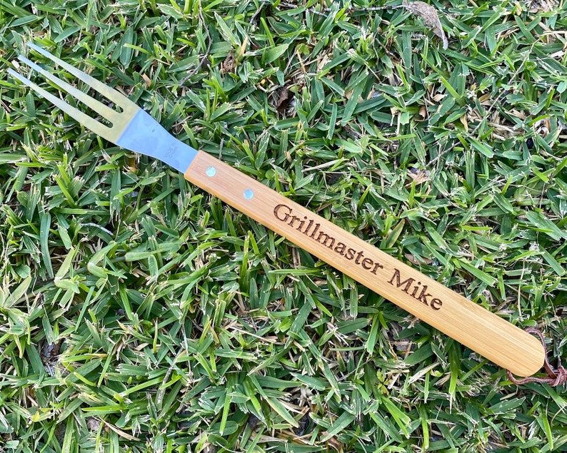 Puede incluir: Un tenedor para asar con mango de madera y p&uacute;as de acero inoxidable. El mango est&aacute; grabado con el texto "Grillmaster Mike".