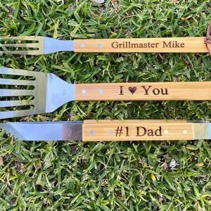 Puede incluir: Un juego de tres herramientas para asar a la parrilla con mangos de madera. Los mangos est&aacute;n grabados con el texto "Grillmaster Mike", "I &hearts; You" y "#1 Dad".