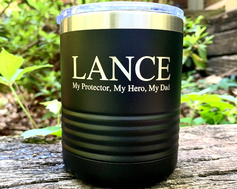 May include: Black stainless steel tumbler with a white inscription that reads "LANCE My Protector, My Hero, My Dad".