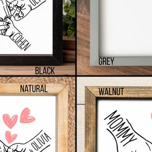 Op de afbeelding: Vier rechthoekige lijsten in zwart, grijs, naturel en walnoot. Elke lijst bevat een witte print met zwarte lijntekeningen van handen die elkaar vasthouden, namen zoals Cohen, Olivia en Mommy, en roze hartillustraties op sommige prints.