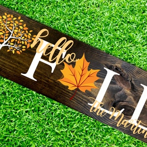 May include: Wooden sign with the text "hello fall the Martins" in white lettering. The sign features a fall-themed design with a yellow and orange tree and a red maple leaf.
