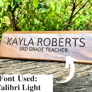 May include: A wooden desk nameplate with the text "KAYLA ROBERTS 3RD GRADE TEACHER" engraved in a Calibri Light font.