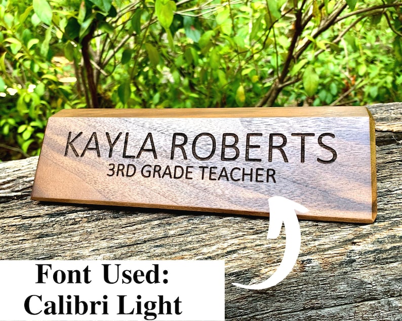 May include: A wooden desk nameplate with the text "KAYLA ROBERTS 3RD GRADE TEACHER" engraved in a Calibri Light font.