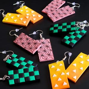 Puede incluir: Una colección de pendientes rectangulares en varios colores y patrones. Los pendientes presentan diseños como formas geométricas, patrones de tablero de ajedrez y triángulos. Los colores incluyen rosa, amarillo, naranja, negro y verde. Cada pendiente tiene un gancho plateado.