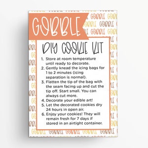 May include: A light orange and white card with the text "GOBBLE DIY COOKIE KIT" and instructions for decorating cookies. The card is surrounded by a pattern of the word "GOBBLE" in orange and yellow.