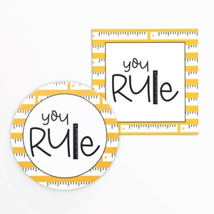 May include: Two round stickers with a yellow and black ruler pattern. The text "you rule" is written in black with a ruler graphic next to it.