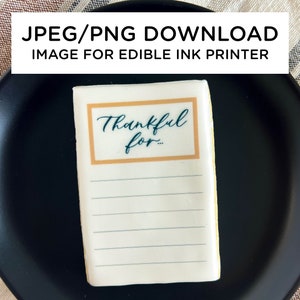 May include: A white rectangular cookie with a gold border and the text "Thankful for..." printed in dark blue. The cookie is on a black plate.
