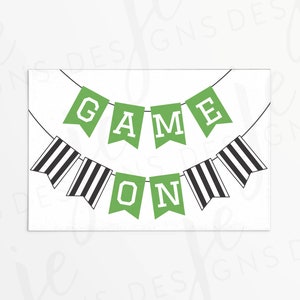 May include: A white card with two banners. The top banner is green with white letters spelling "GAME". The bottom banner is green with white letters spelling "ON". The bottom banner has black and white striped flags.