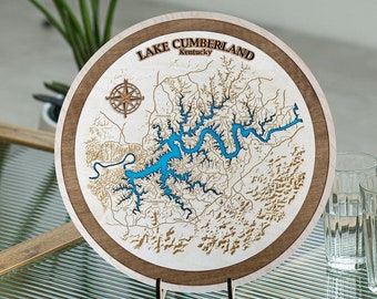 May include: A wooden map of Lake Cumberland, Kentucky, with a compass and blue water features. The map is mounted on a wooden stand.