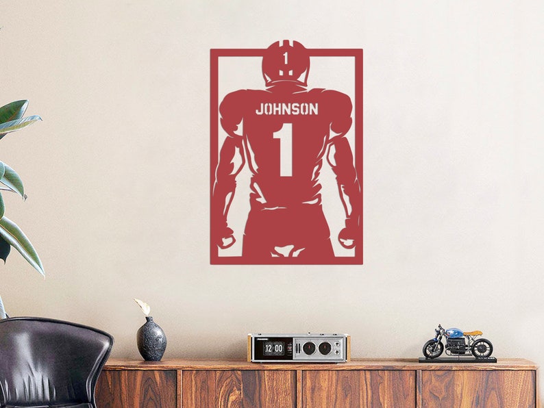 Pu&ograve; includere: Silhouette rossa di un giocatore di football americano che indossa una maglia con il nome "JOHNSON" e il numero "1". La silhouette &egrave; incorniciata in un rettangolo rosso.
