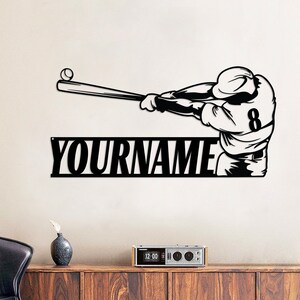 Pu&ograve; includere: Arte da parete in metallo nero con un giocatore di baseball che oscilla una mazza con la palla in aria. L'opera d'arte include il testo "YOURNAME" sotto il giocatore.