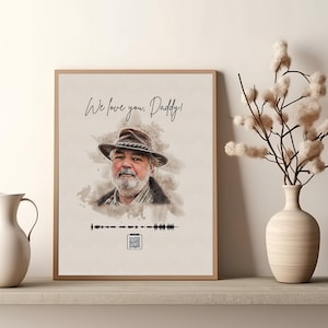 May include: A framed print featuring a watercolor portrait of a man wearing a hat. The text "We love you, Daddy!" is above the portrait. Below the portrait is a sound wave graphic and a QR code. The frame is a light brown color.
