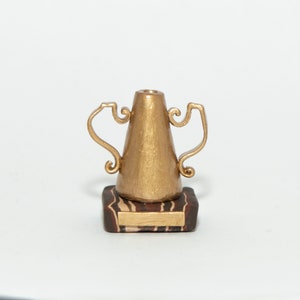 May include: A gold trophy with a cone-shaped base and two handles. The trophy is sitting on a brown and black striped base.