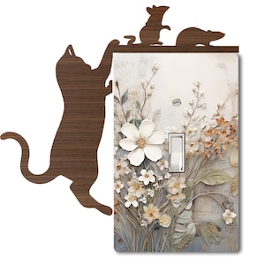 May include: A light switch cover with a floral design featuring white flowers and brown leaves. A wooden silhouette of a cat reaching up towards the switch cover and two mice on top of the switch cover.