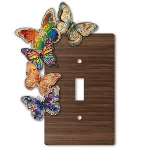 Puede incluir: Una placa de pared para interruptor de luz rectangular con un acabado de grano de madera marrón oscuro. Cinco mariposas decorativas de varios colores, incluyendo arcoíris, naranja, azul y amarillo, están dispuestas en el lado izquierdo.