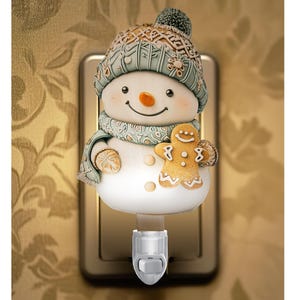 May include: A whimsical snowman night light with a smiling face, wearing a patterned hat and scarf. The snowman holds a gingerbread man. The night light plugs into a wall outlet and has an on/off switch.
