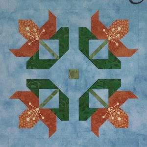 Pode incluir: Um bloco de colcha com um design simétrico apresentando quatro flores laranja com folhas verdes sobre um fundo azul claro.