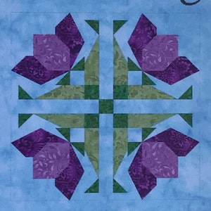 May include: A quilt block with a blue background and a design of four purple flowers with green leaves. The flowers are arranged in a cross pattern.