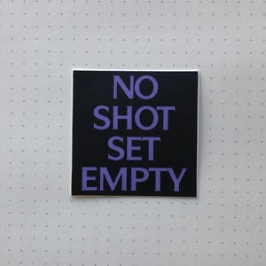Könnte beinhalten: Schwarzer Aufkleber mit weißem Text, der "NO SHOT SET EMPTY" in lila Schrift lautet.