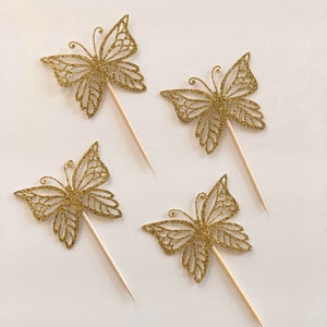 Pu&ograve; includere: Quattro decorazioni per torte a forma di farfalla dorata con glitter e bastoncini di legno. I ritagli di farfalle presentano intricati disegni alari. Ideali per torte, cupcake o altre prelibatezze festive.