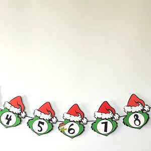 Pode incluir: Uma faixa de Natal com rostos do Grinch usando chap&eacute;us de Papai Noel, numerados de 1 a 12. O rosto verde do Grinch e o chap&eacute;u vermelho com borda branca s&atilde;o proeminentes. Ideal para um calend&aacute;rio do Advento.