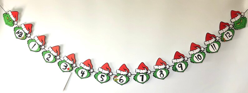 Pode incluir: Uma faixa de Natal com rostos do Grinch usando chap&eacute;us de Papai Noel, numerados de 1 a 12. O rosto verde do Grinch e o chap&eacute;u vermelho com borda branca s&atilde;o proeminentes. Ideal para um calend&aacute;rio do Advento.