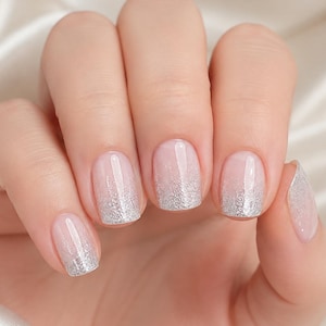 Könnte beinhalten: Fingernägel mit einer transparenten Grundierung und einem silbernen Glitzerverlauf, der an den Spitzen beginnt und zur Mitte jedes Nagels hin verblasst. Die Nägel sind abgerundet geformt und haben ein glattes, glänzendes Finish.