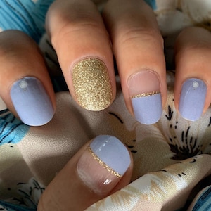 May include: Close-up of a hand with five fingernails painted in a light blue color with a gold accent. One fingernail is painted with gold glitter.