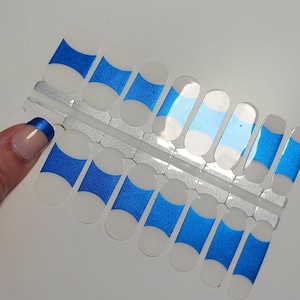 May include: A sheet of nail wraps featuring a design of white and blue curved stripes. The nail wraps are on a clear plastic backing. A fingernail with a blue tip is visible.